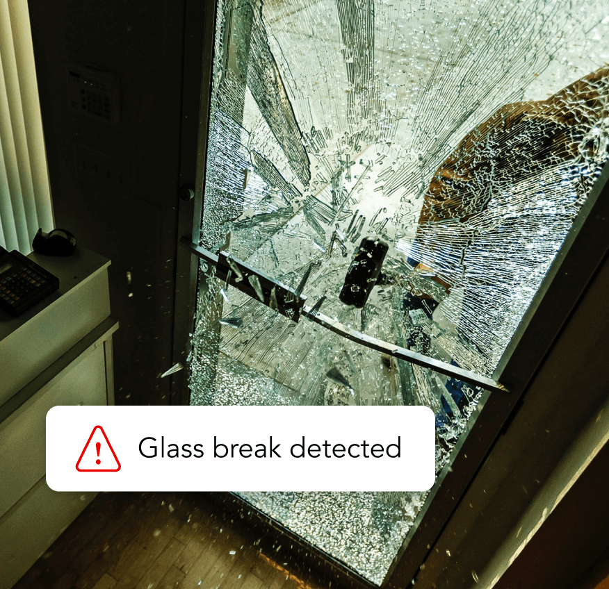 A connected security system in action. An environmental monitor E50 detects the sound of breaking glass as an intruder enters. The device measures and analyzes the acoustic signature, triggering an alert notification to security personnel. The smart sensor is mounted on a rack alongside other components, showcasing its integration into a comprehensive environmental monitoring setup that also measures factors like airflow, temperature, humidity, vape, particulate matter and more.