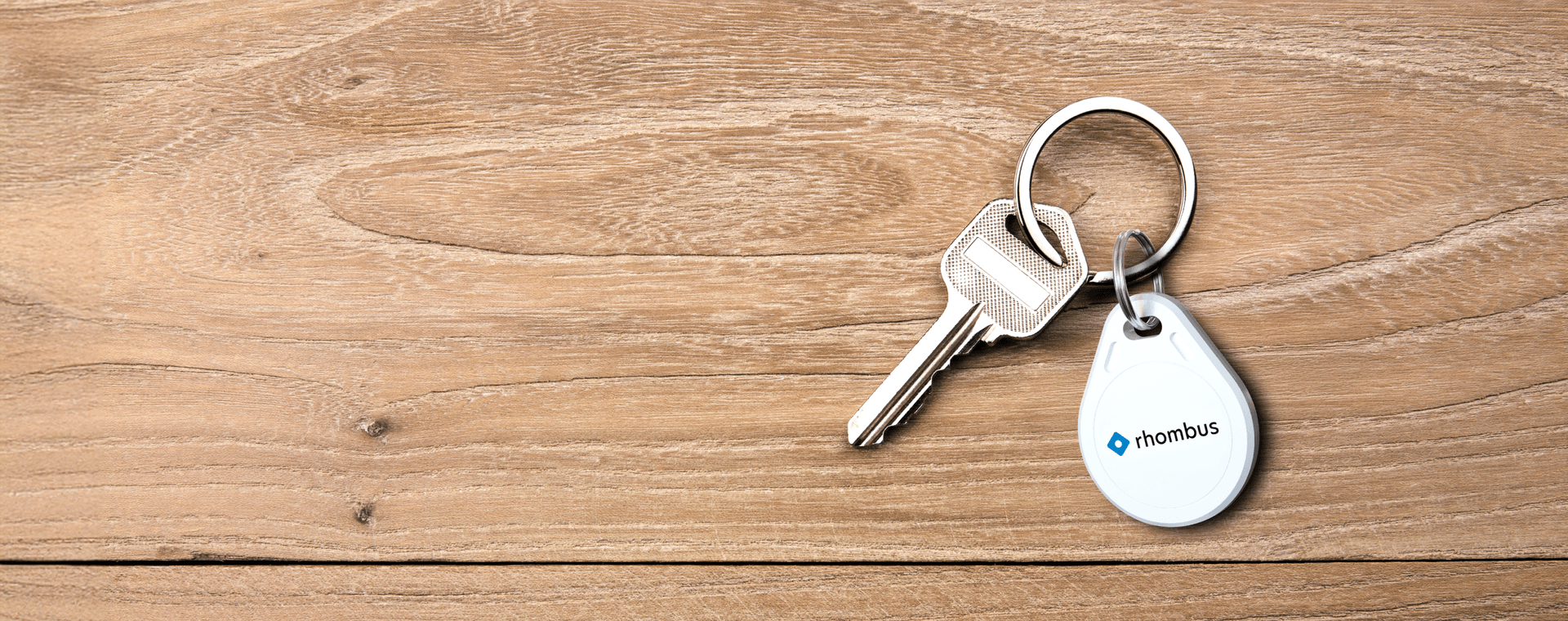 A white key fob featuring the word "Rhombus" in bold text and key chain set against a wood background.